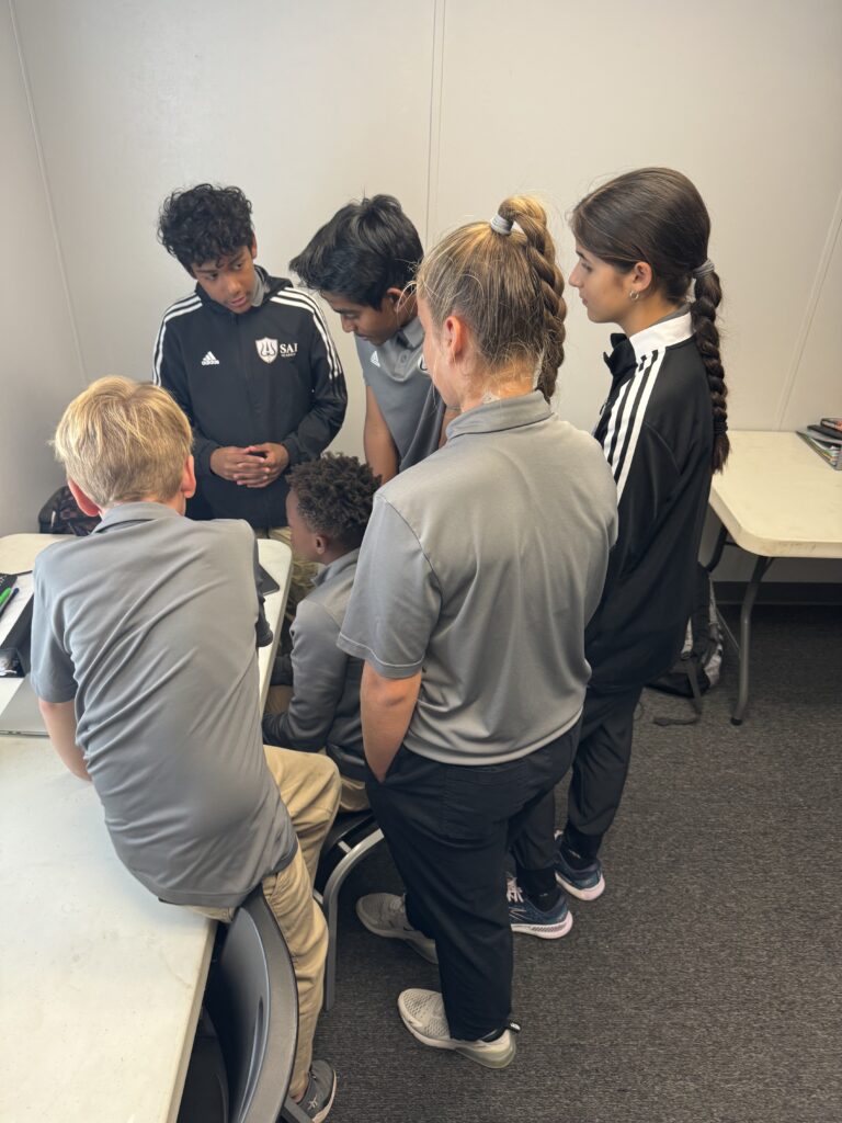 A group of students in athletic gear gather around a seated person, engaged in a discussion in a classroom setting. This scene captures the essence of teamwork and learning, perfect for showcasing on your homepage to boost SEO with relevant and important keywords.